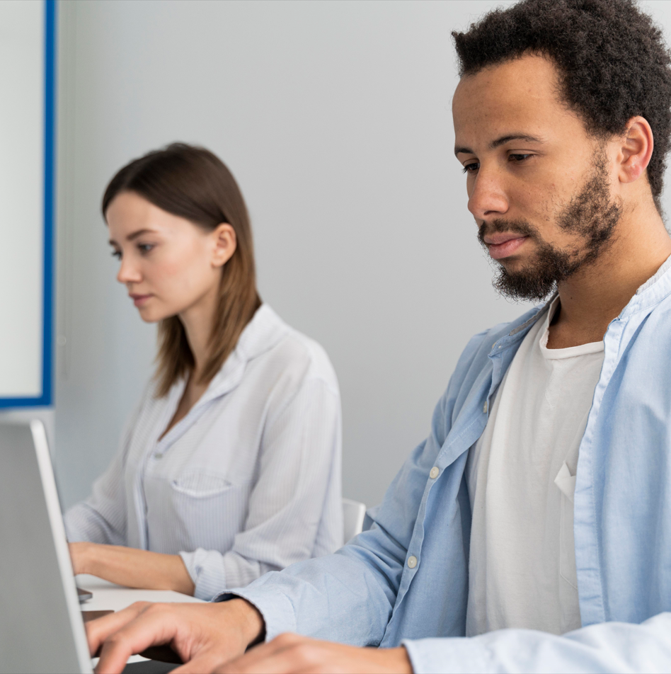 deux personnes concentrées en train de travailler sur leurs ordinateurs dans un environnement de bureau professionnel, suggérant une séance de travail ou de formation